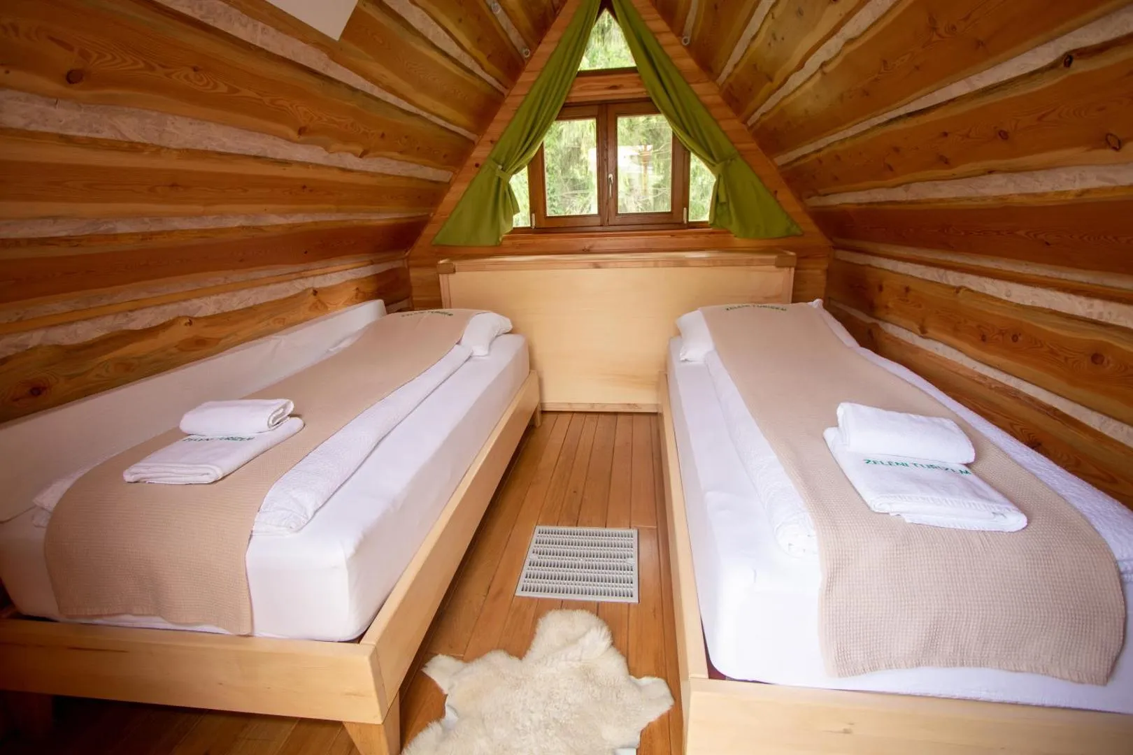 Notranjost glamping hiške: pogrnjena postelja pod strmim macesnovim ostrešjem.