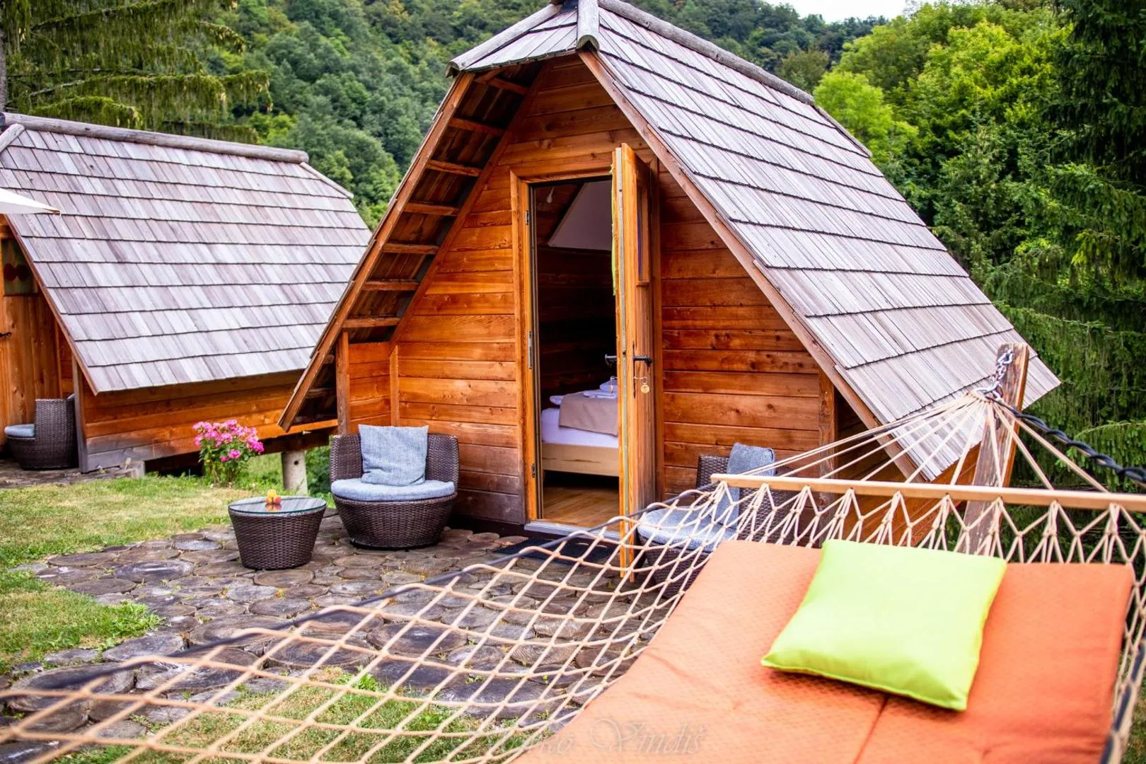 Macesnova glamping hiška s svojo majhno teraso med drevesi.