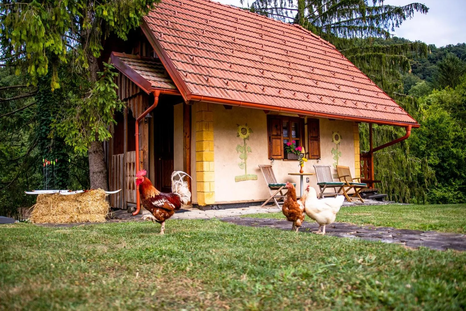 Zunanjost pastirske koče: poslikan cvetlični omet na glinenih stenah med drevesi.