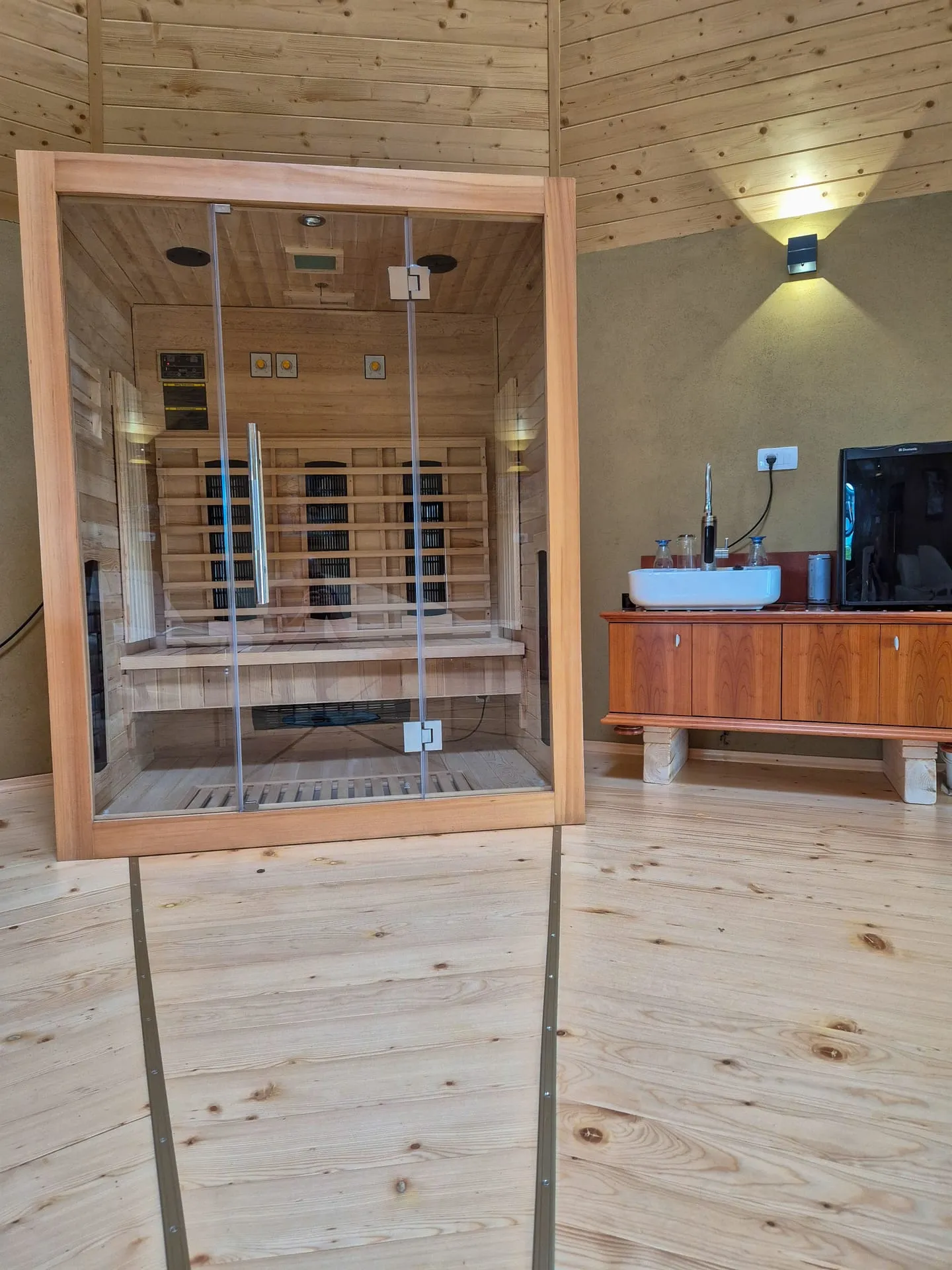 Infrared sauna cabin with glass door in a warm-lit wooden room.